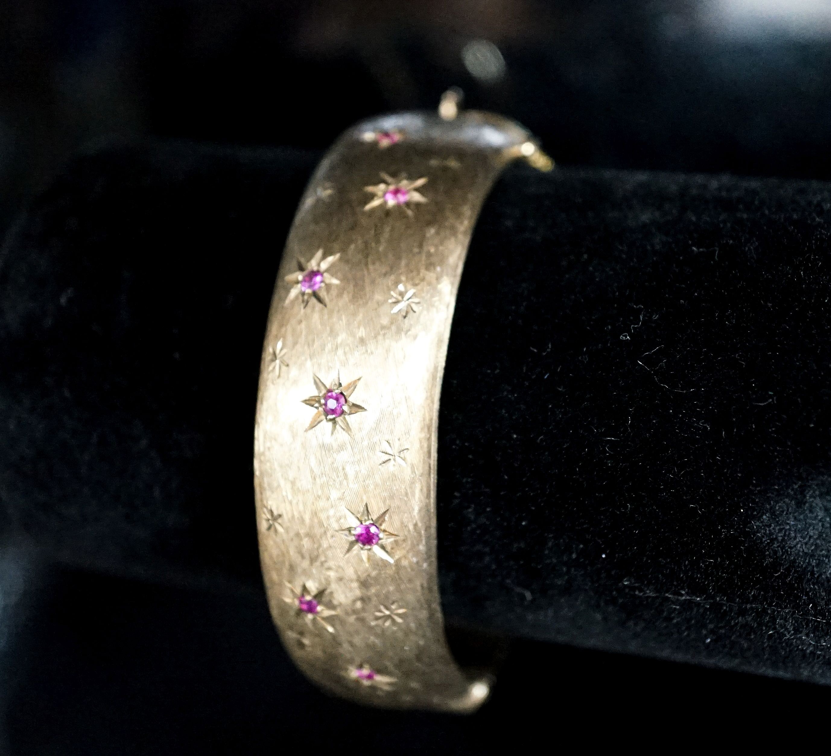 A 1960's engraved 9ct gold and ruby set hinged bracelet, interior diameter 58mm, gross weight 35.7 grams.